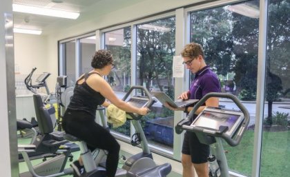 Woman on exercise bike while man stands nearby with laptop. Supplied.